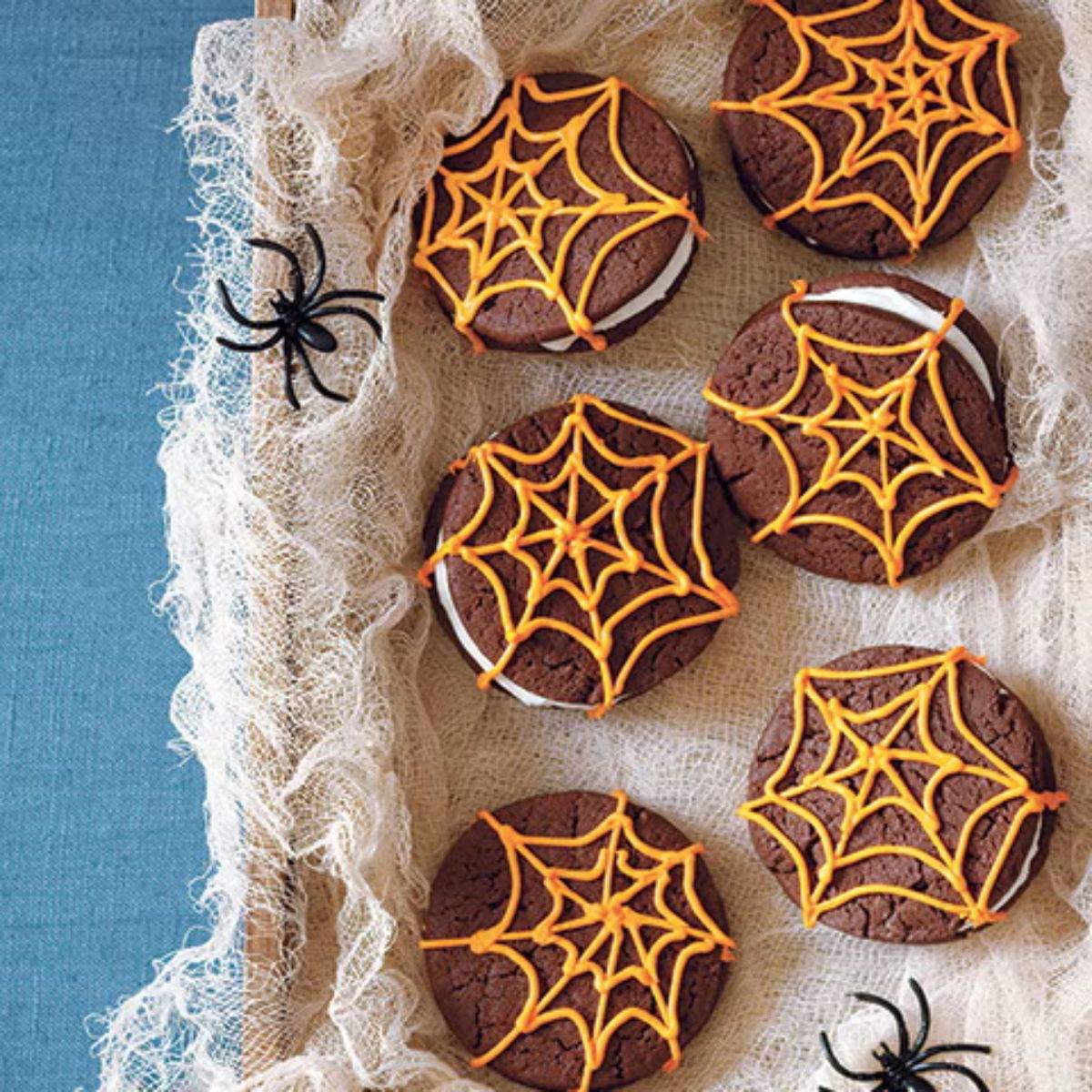 Chocolate sandwich cookies decorated with orange icing spider webs as a Halloween party food idea