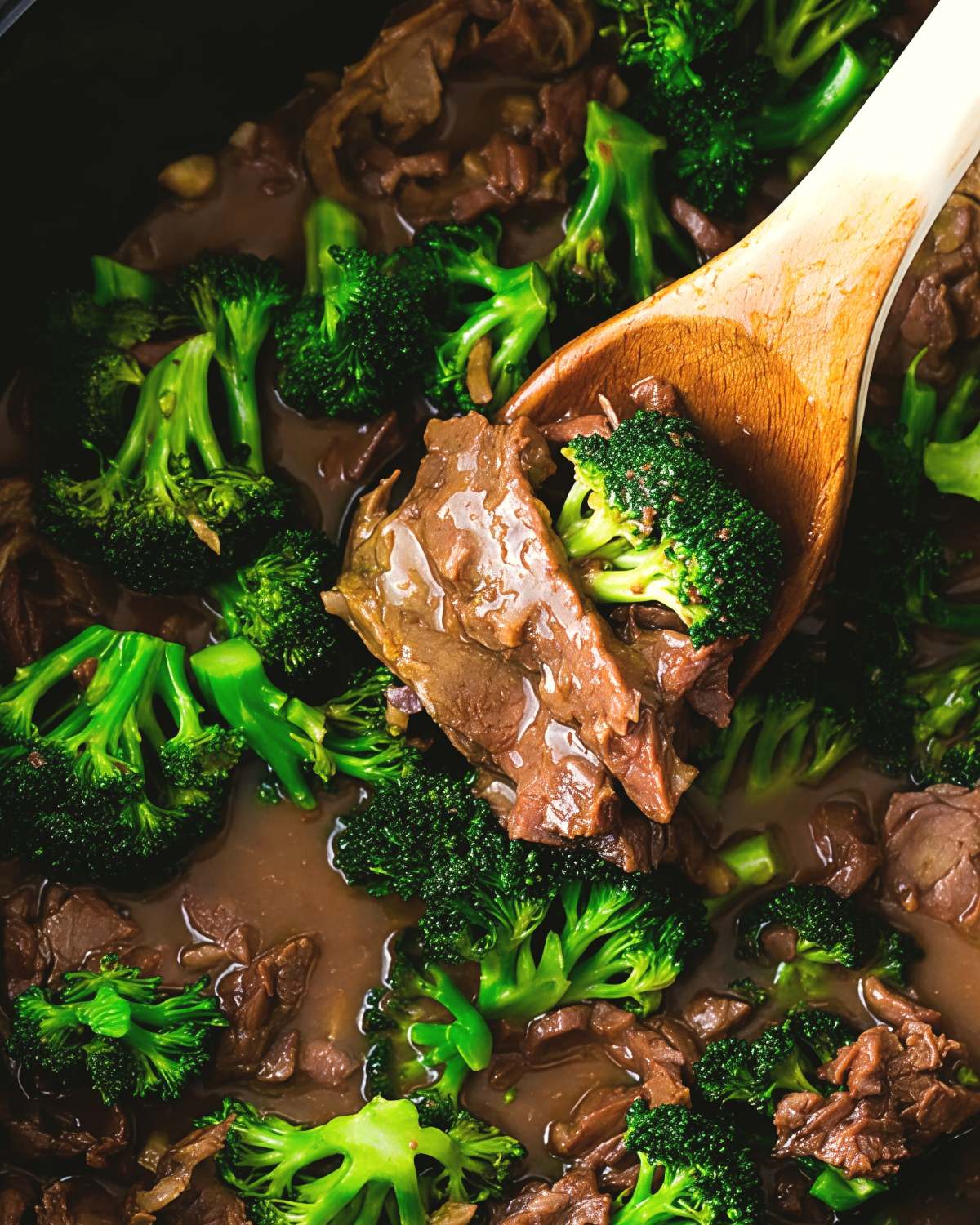 Healthy slow cooker beef and broccoli in a savory sauce with a wooden serving spoon.