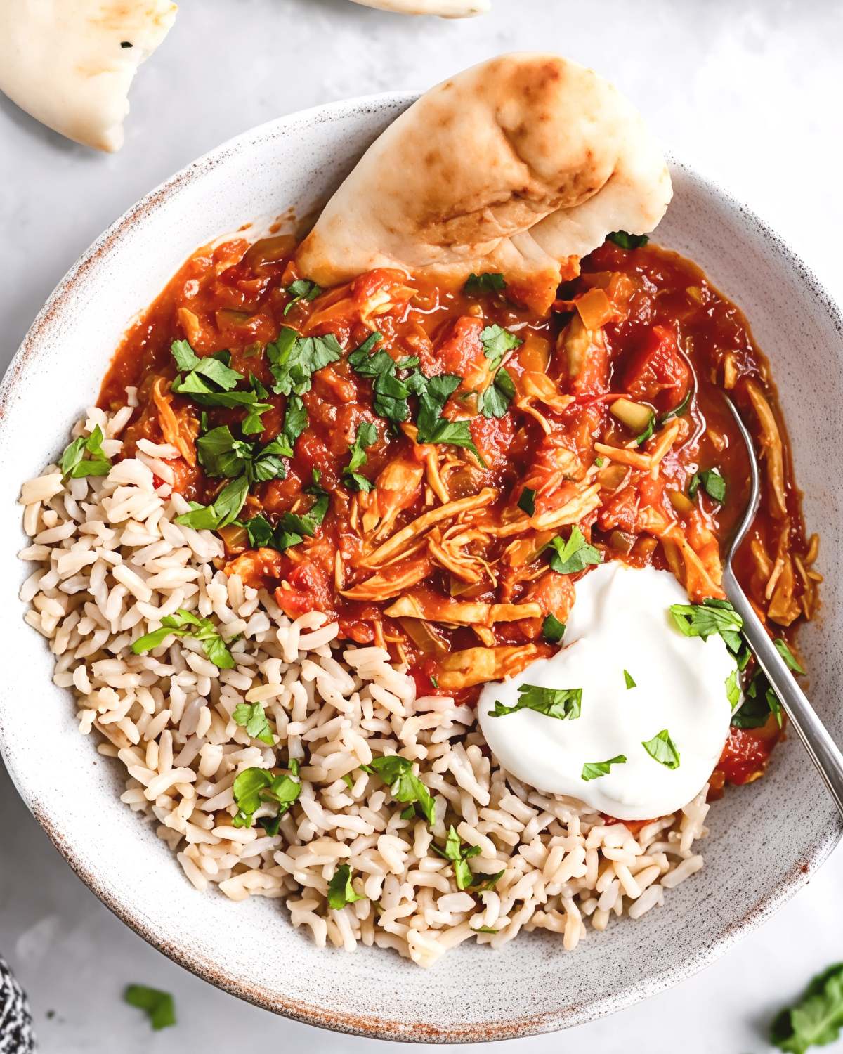 Healthy slow cooker chicken tikka masala served with brown rice, a dollop of yogurt, fresh cilantro, and naan