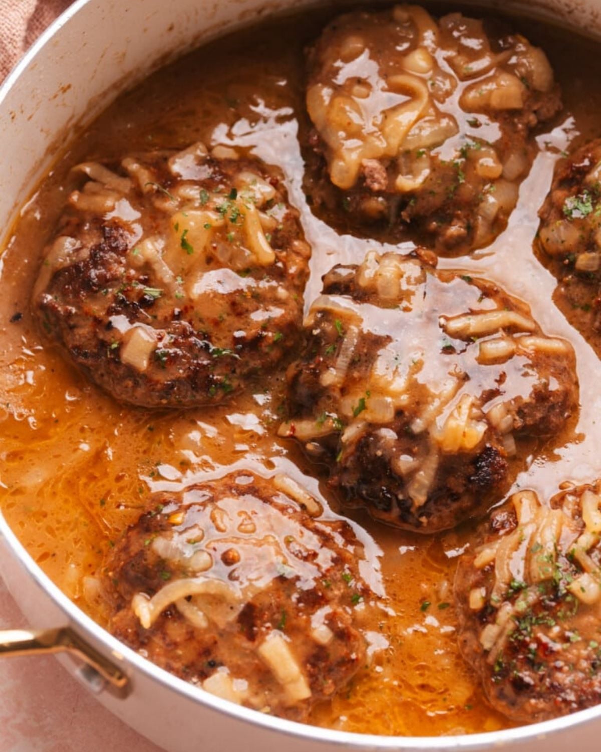 Easy old fashioned Salisbury steak patties simmering in onion gravy in a skillet for a quick ground beef dinner recipe