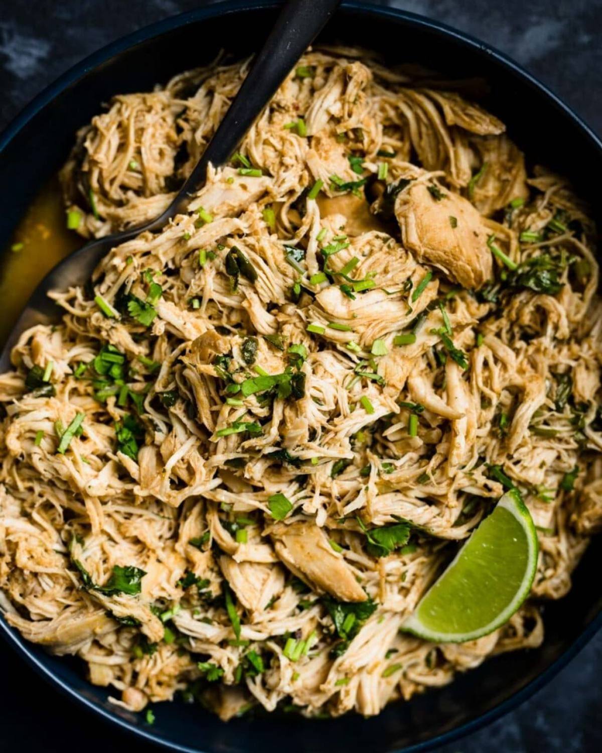 Slow-Cooker Cilantro Lime Chicken shredded in a dark bowl with a lime wedge and a serving spoon