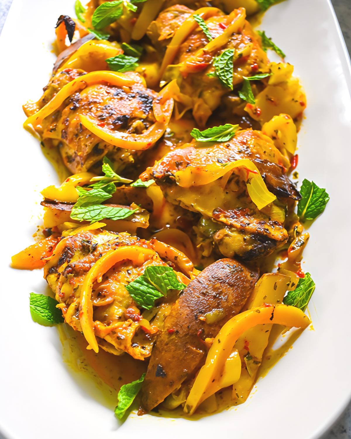 Slow cooker Moroccan spiced chicken thighs served on a white platter, garnished with sliced yellow peppers and fresh mint leaves.