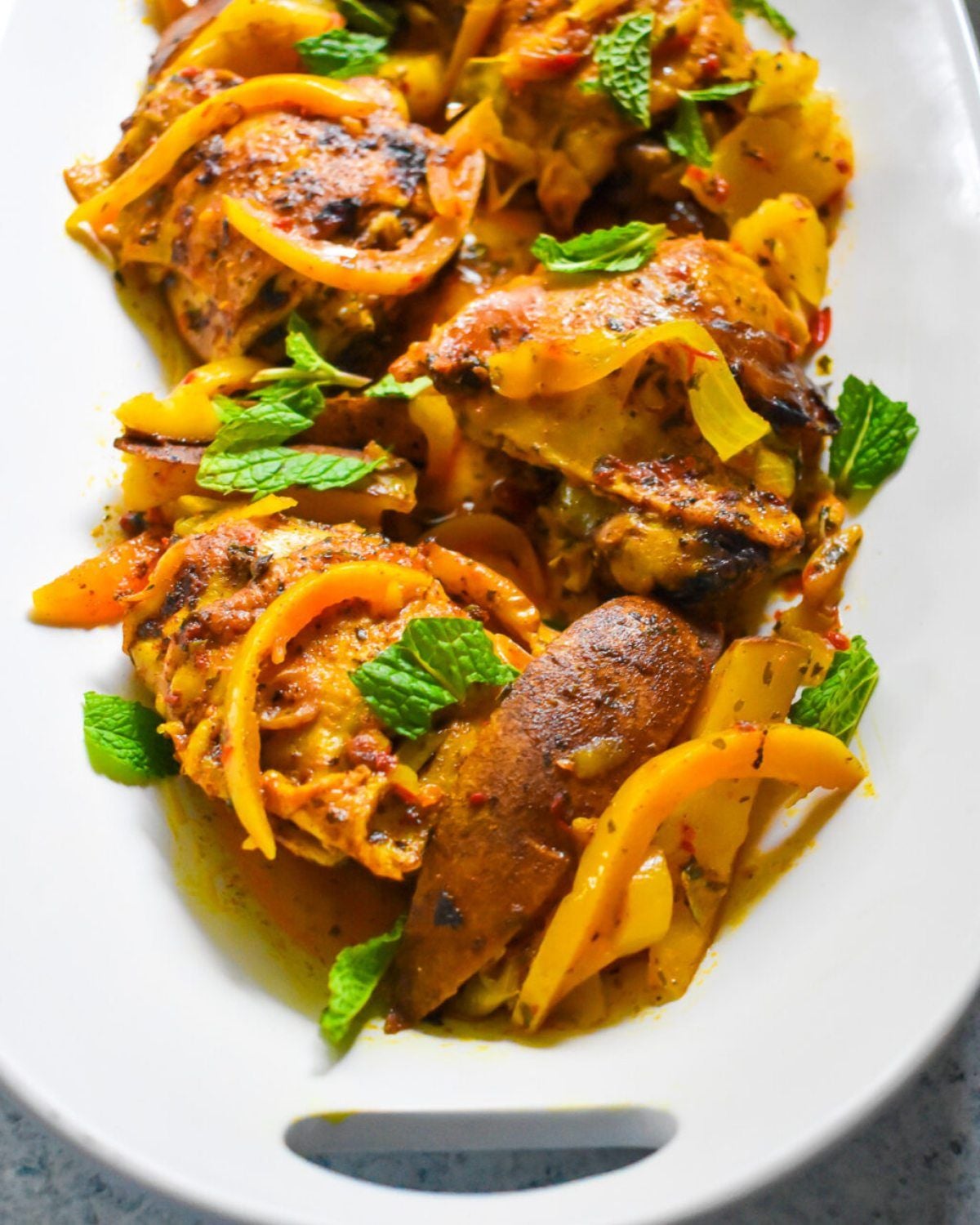 Slow-Cooker Moroccan Spiced Chicken Thighs served on a white platter with yellow bell peppers and fresh mint