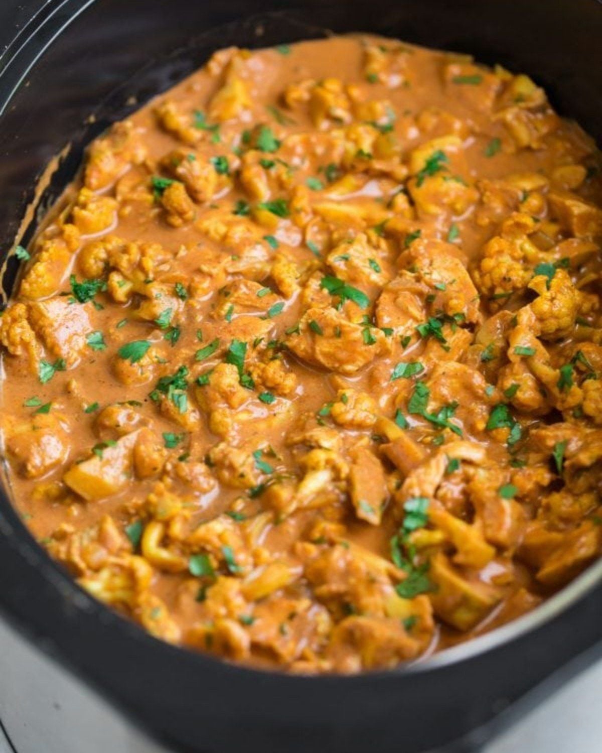 Slow cooker high protein butter chicken in a crockpot garnished with fresh parsley.