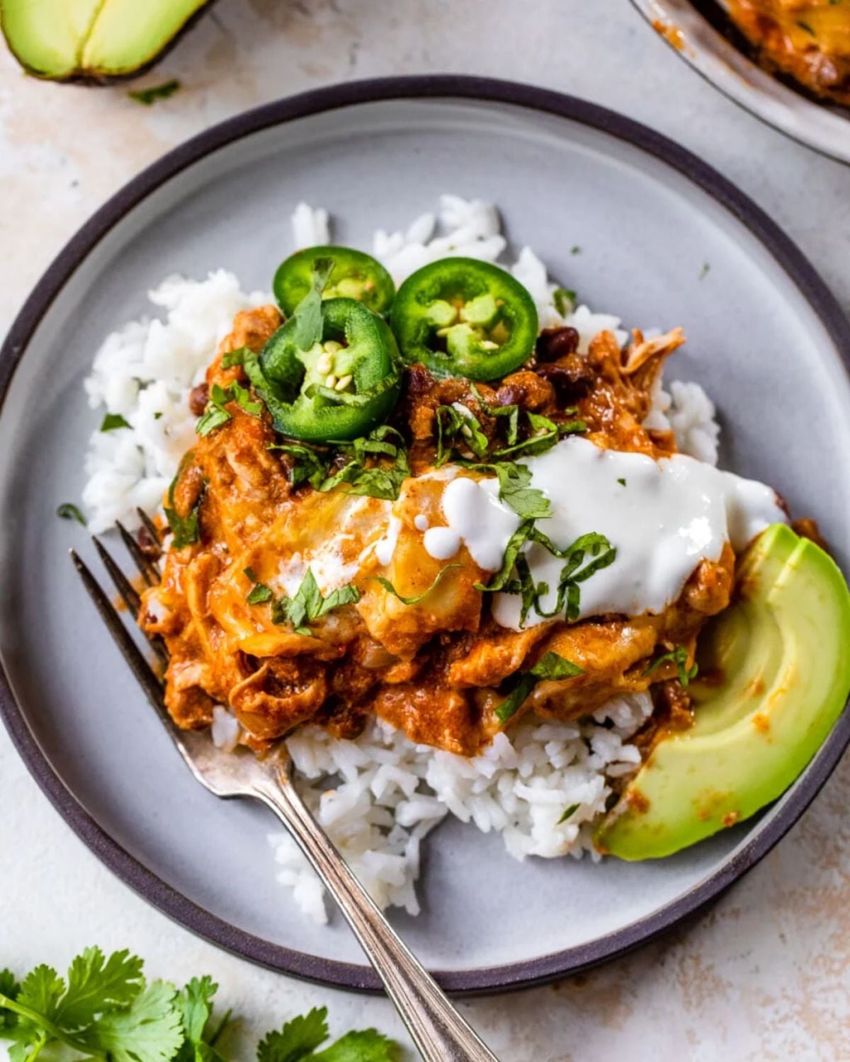 Slow cooker high protein chicken enchiladas served over white rice with sour cream, sliced jalapeños, and avocado on a plate.