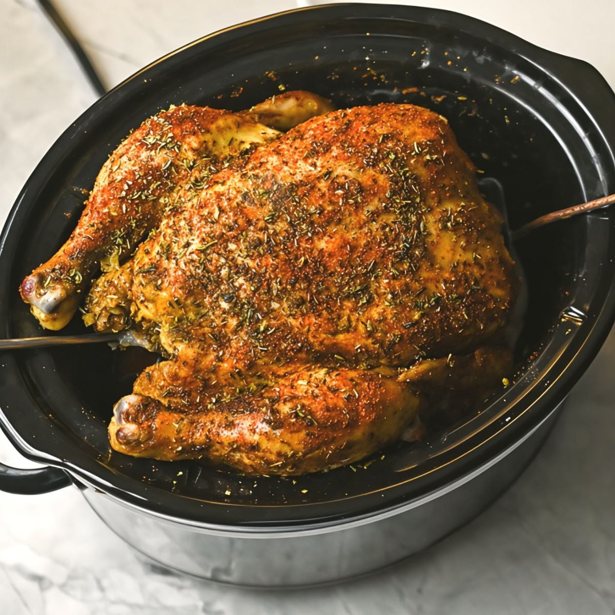 A whole seasoned chicken cooked inside a black slow cooker.