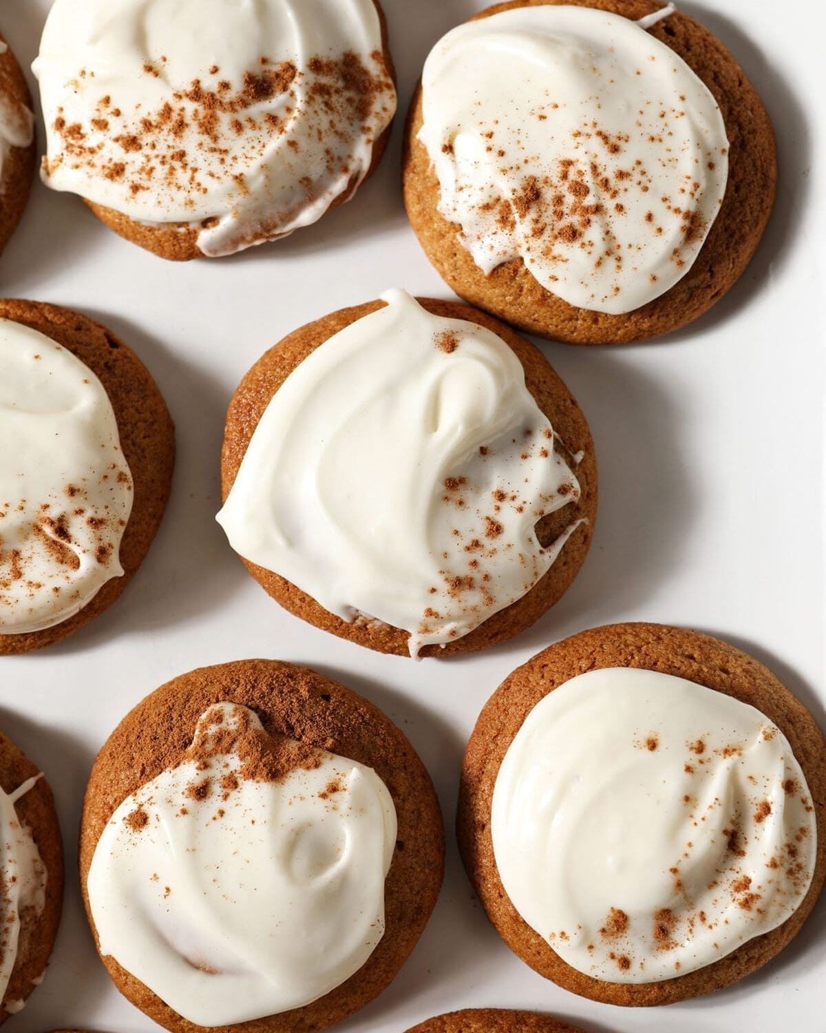 Soft pumpkin drop cookies spread with white cream cheese frosting and dusted with cinnamon, arranged on a white platter.