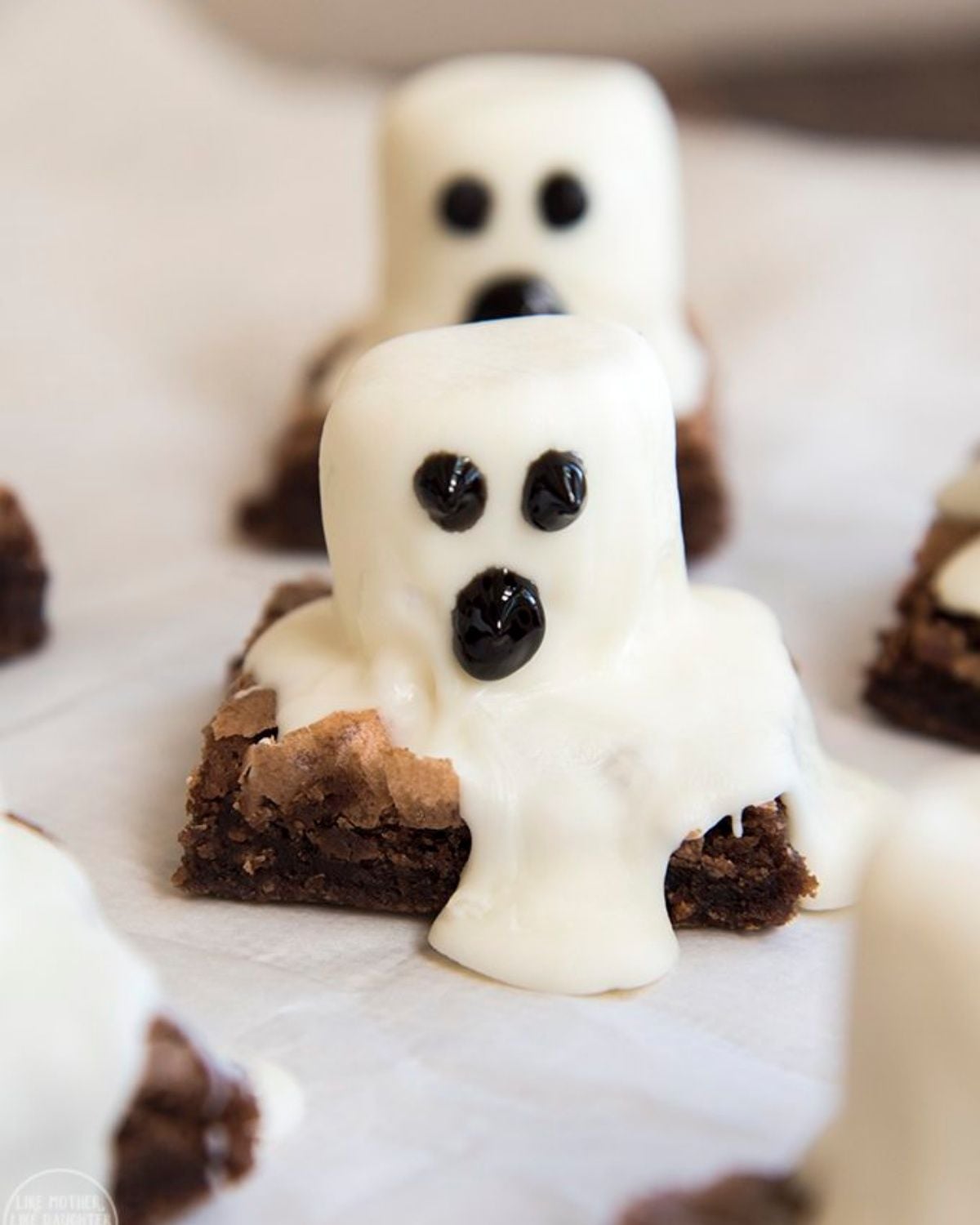 Fudgy ghost brownies topped with marshmallow ghosts and black decorating gel faces, perfect for a fun Halloween treat for kids school.