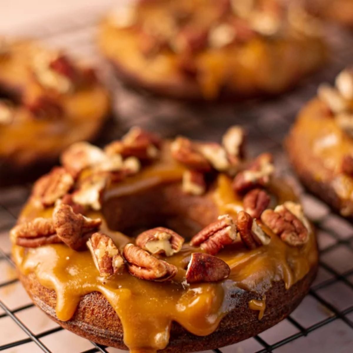 Healthy fall dessert glazed donuts topped with caramel and chopped pecans on a wire cooling rack