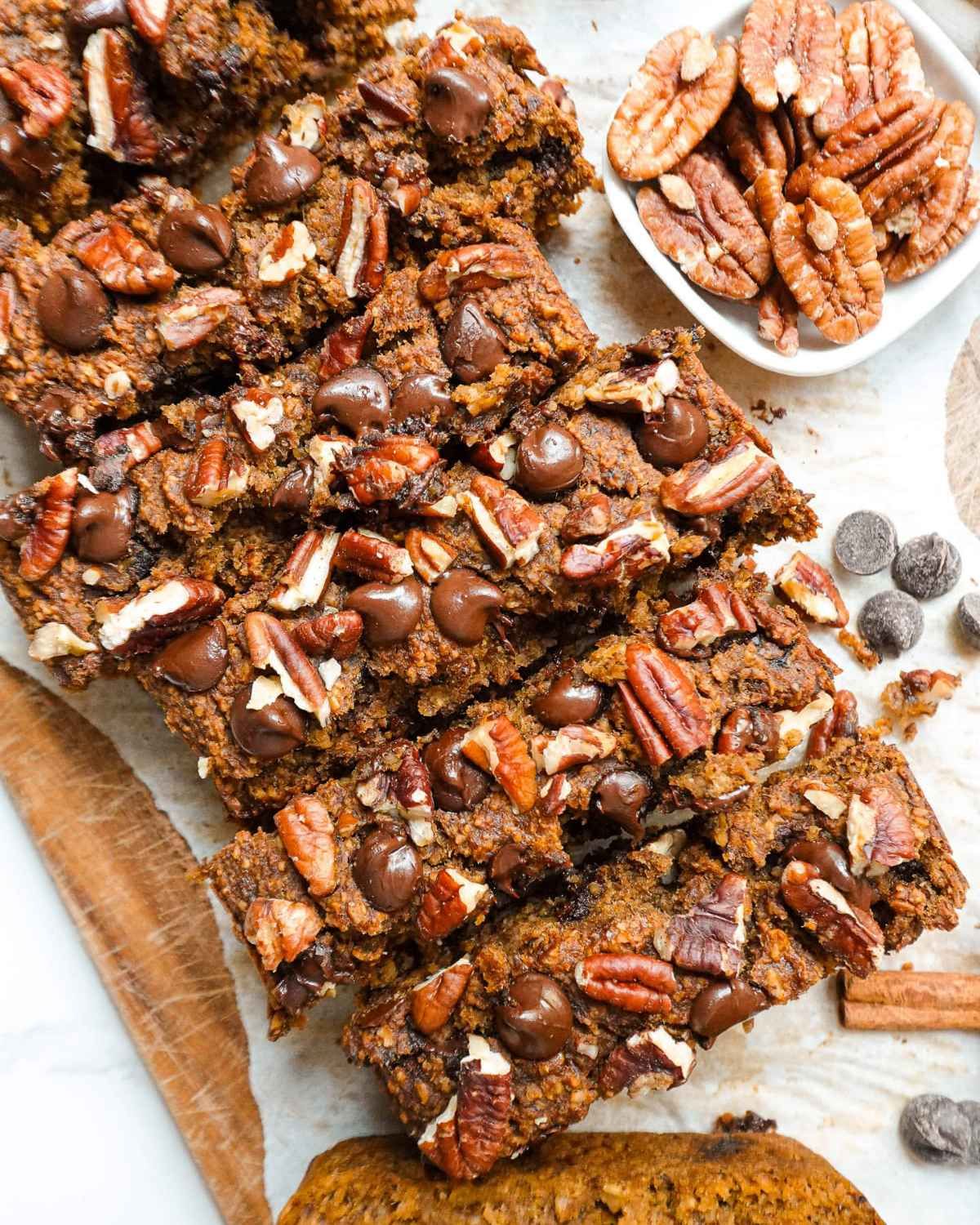 Healthy fall dessert sliced banana bread topped with pecans and chocolate chips next to a bowl of pecans