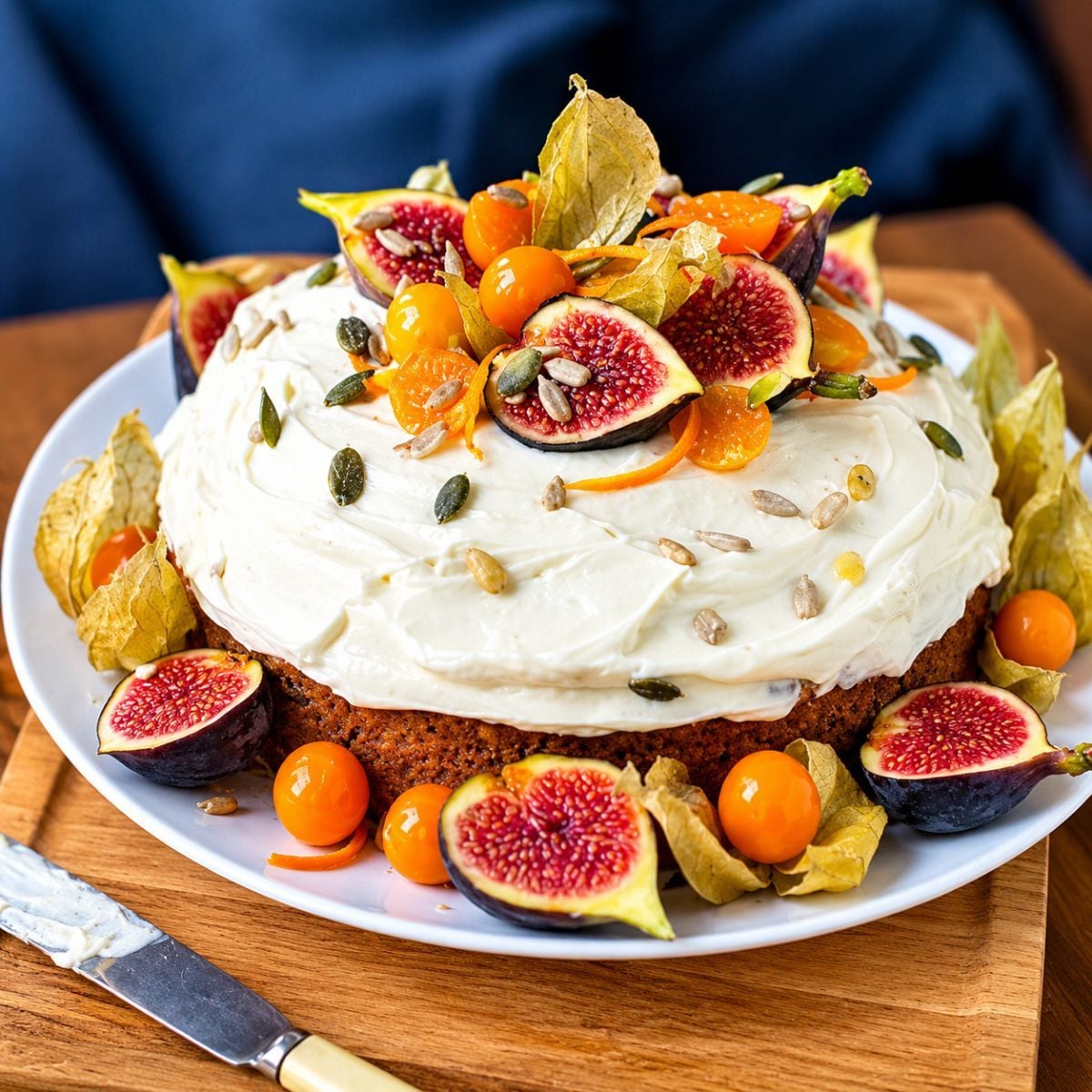 Healthy fall dessert carrot cake with white frosting, fresh figs, physalis berries, and seeds on a white plate