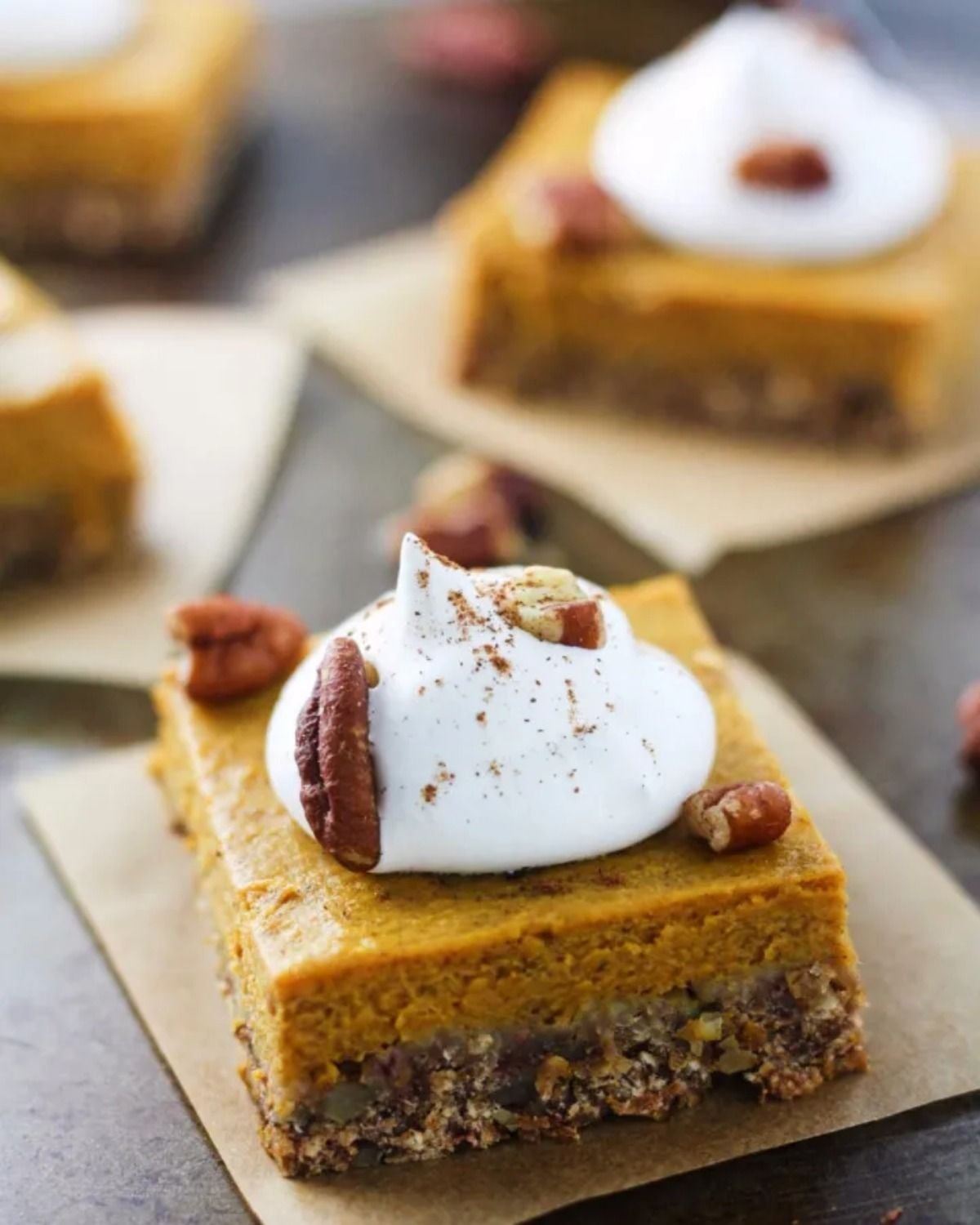 Healthy fall dessert pumpkin pecan bars topped with whipped cream and pecans on parchment paper