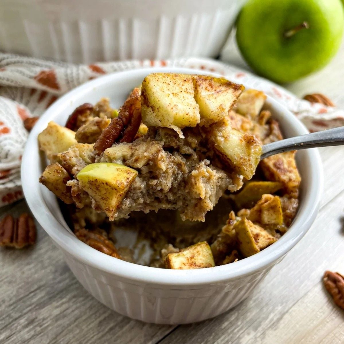Healthy fall dessert apple pie baked vegan protein oatmeal in a white ramekin with a spoonful being lifted