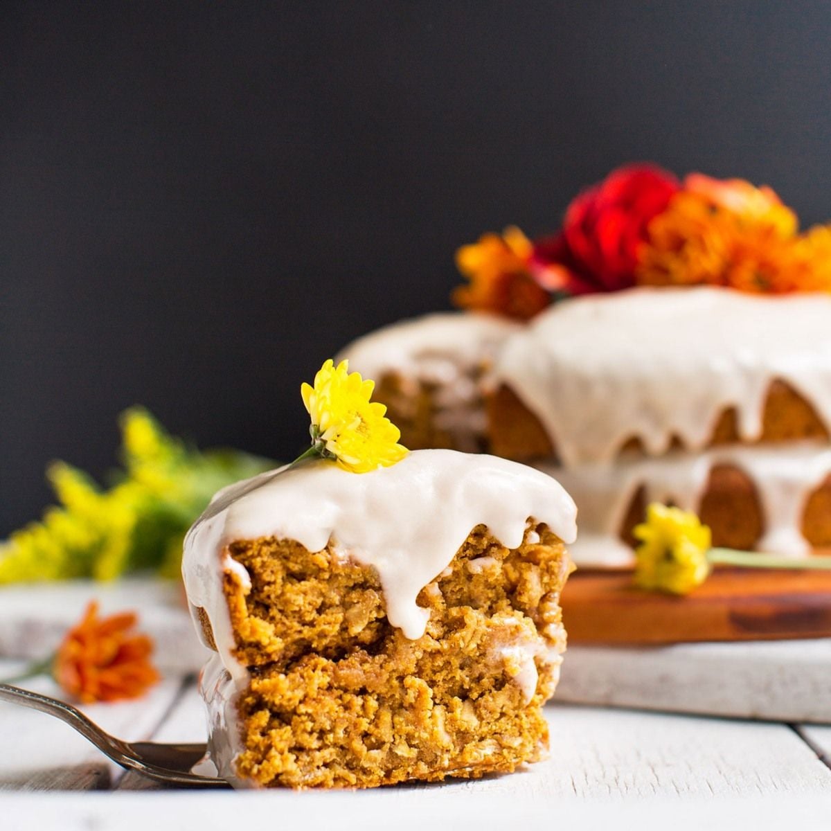 Healthy fall dessert slice of pumpkin cake with white frosting and a yellow flower on top served on a fork