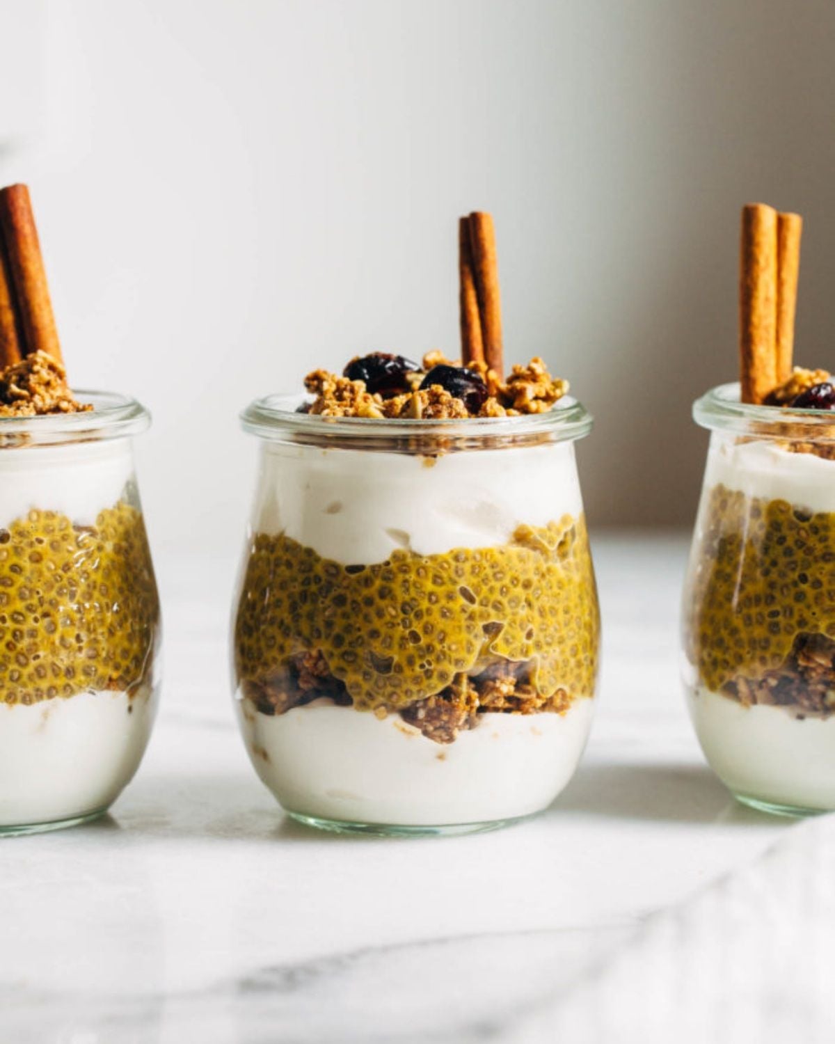 Three small glass jars filled with layered pumpkin chia pudding parfaits as healthy fall desserts
