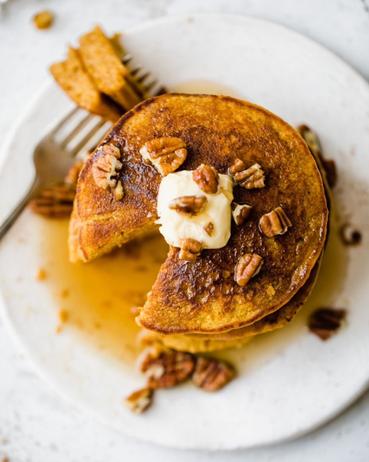 Healthy fall dessert stack of pumpkin pancakes topped with butter, pecans, and syrup on a white plate with a fork