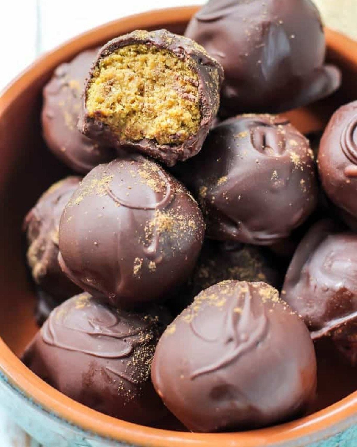 Healthy fall dessert chocolate covered pumpkin truffles in a bowl with one bitten to show the filling