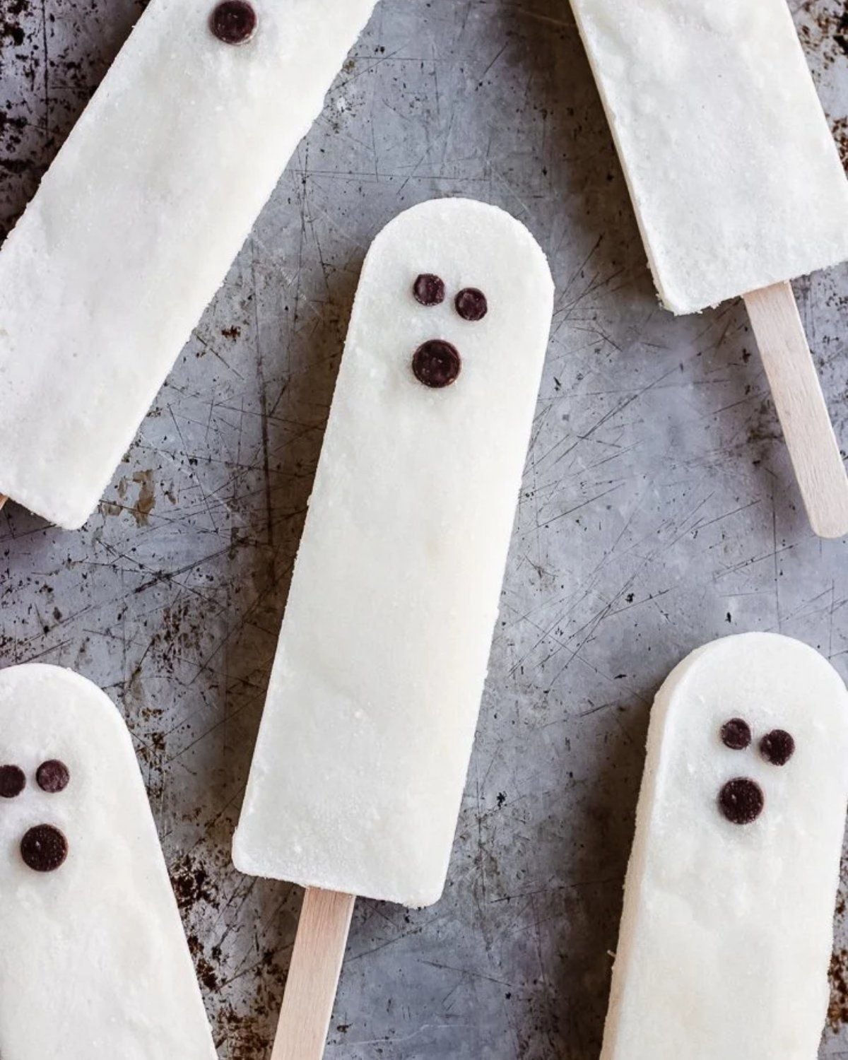 Healthy Halloween treats featuring white ghost popsicles with chocolate chip faces resting on a rustic surface.