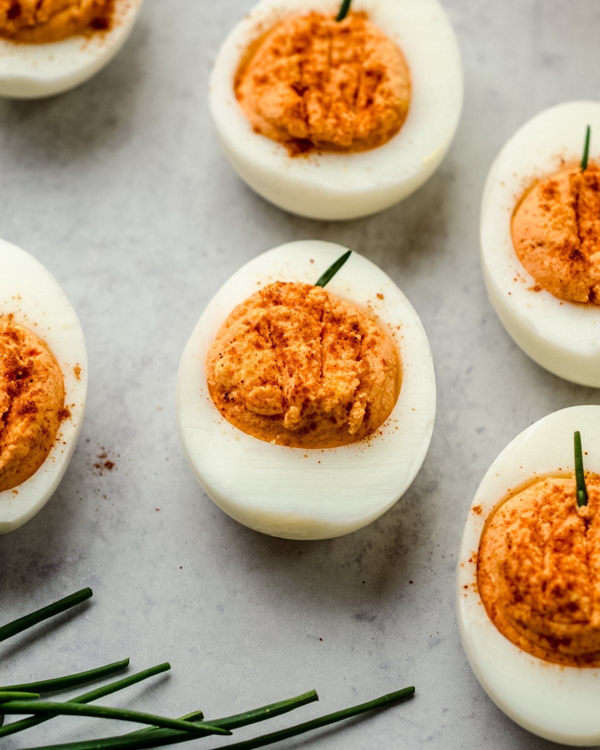 Healthy Halloween treats featuring deviled eggs decorated with chive stems to look like little pumpkins on a light background.