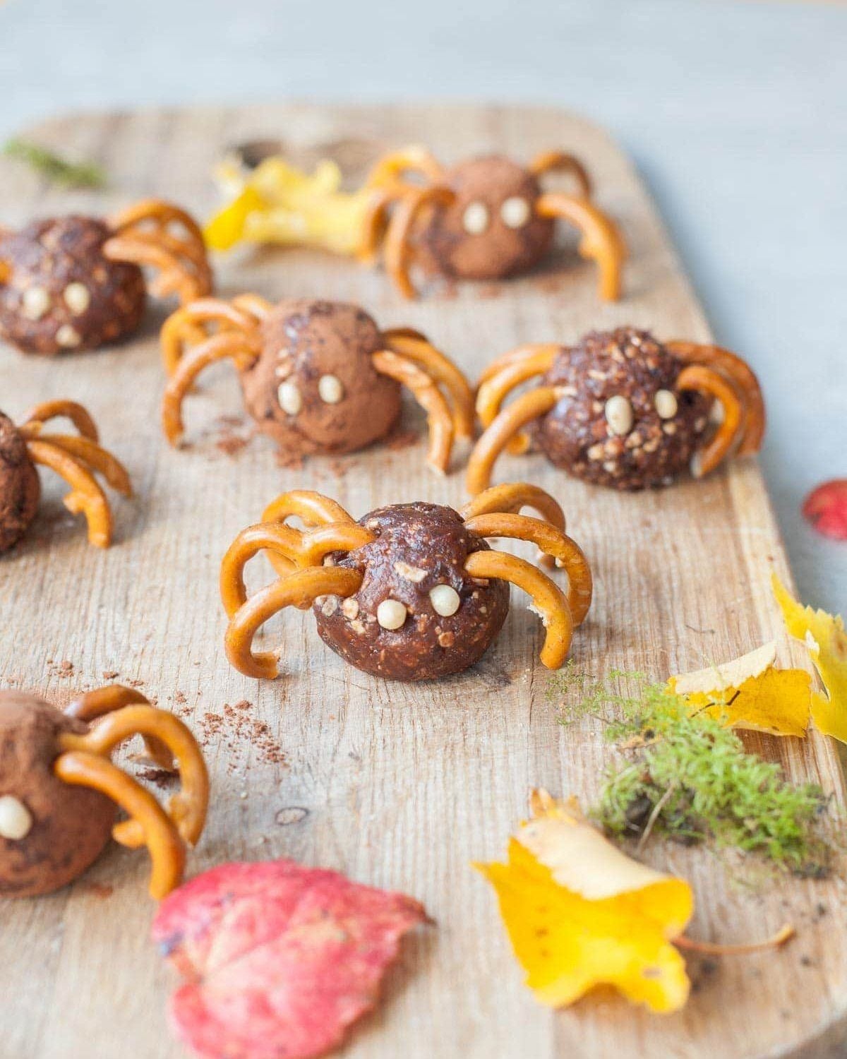Healthy Halloween treats featuring energy bite spiders made with pretzel legs and small candy or seed eyes on a wooden board