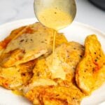 A spoon drizzling creamy sun-dried tomato sauce over skillet marry me chicken on a white plate