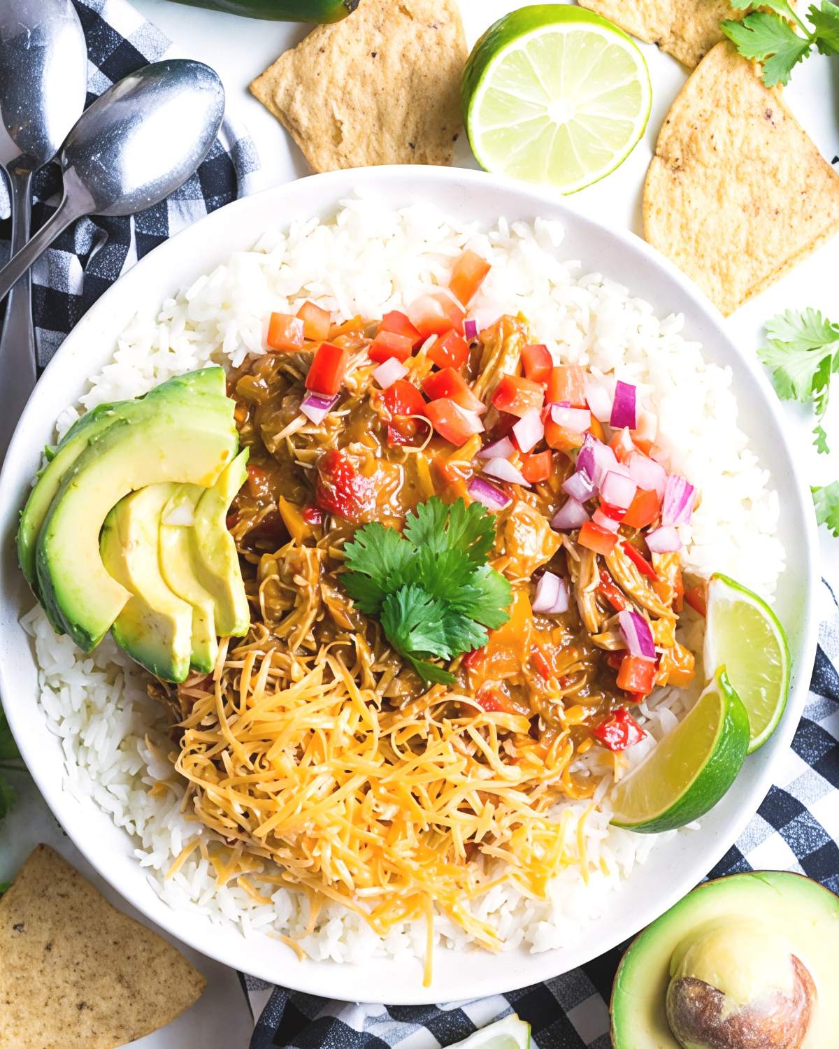 Healthy crockpot pumpkin chicken chili served over white rice with sliced avocado, shredded cheese, cilantro, and diced red onions.