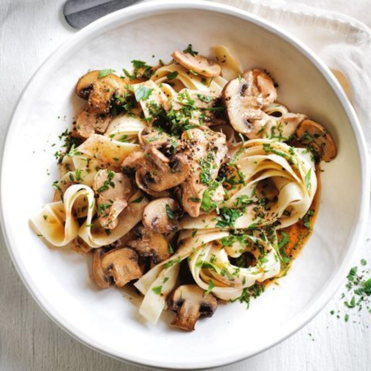 Slow cooker high protein chicken stroganoff with mushrooms and pasta in a white bowl garnished with chopped parsley.