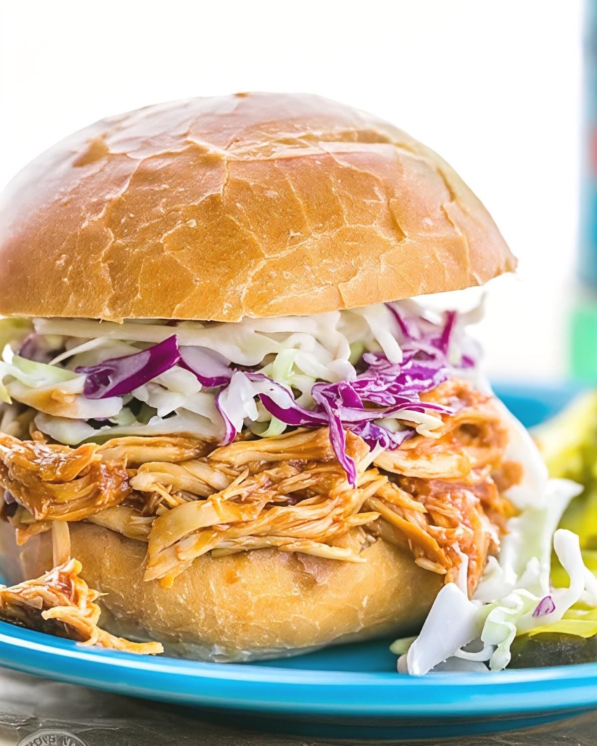 A hearty barbecue pulled chicken sandwich topped with crisp coleslaw on a soft bun, presenting a savory dump and go crockpot dinners chicken recipe.
