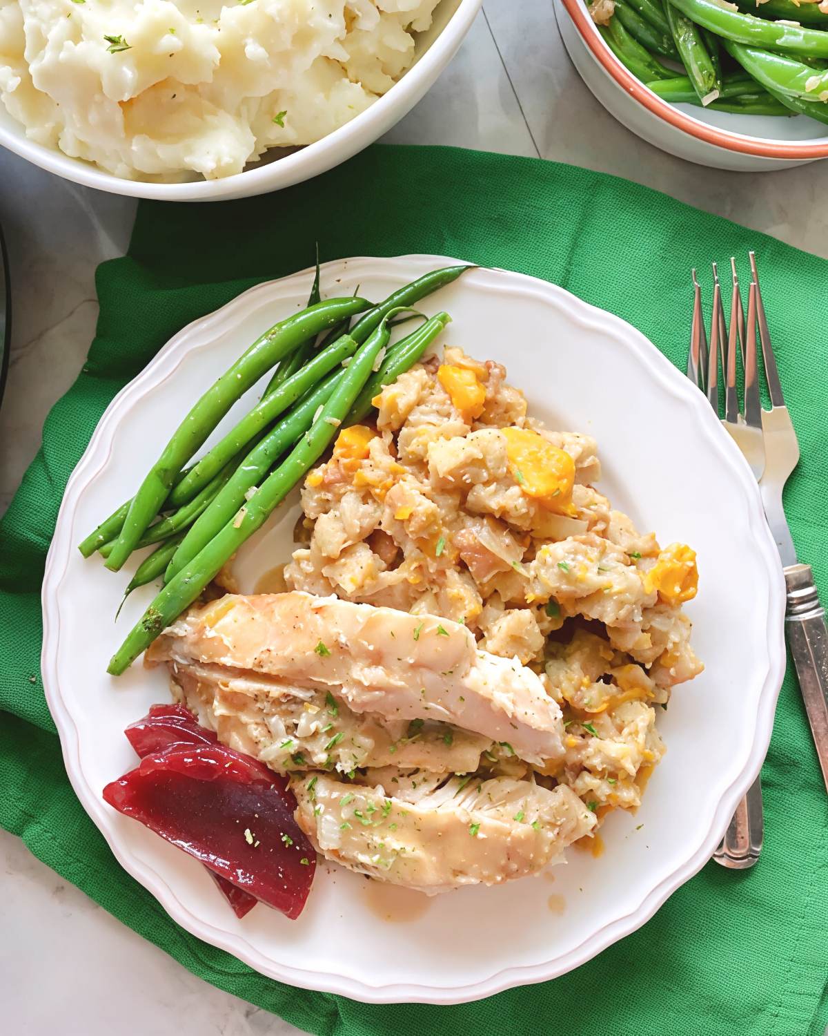 A complete Thanksgiving dinner plate with turkey, green beans, cranberry sauce, and crockpot stuffing thanksgiving recipe set over a green napkin.