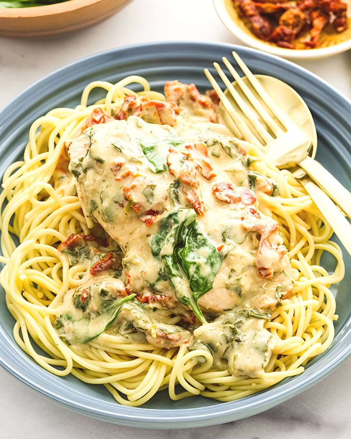 Creamy Tuscan chicken smothered in a rich parmesan sauce with spinach and sun-dried tomatoes served over spaghetti, representing an indulgent dump and go crockpot dinner (Lazy Dinner).