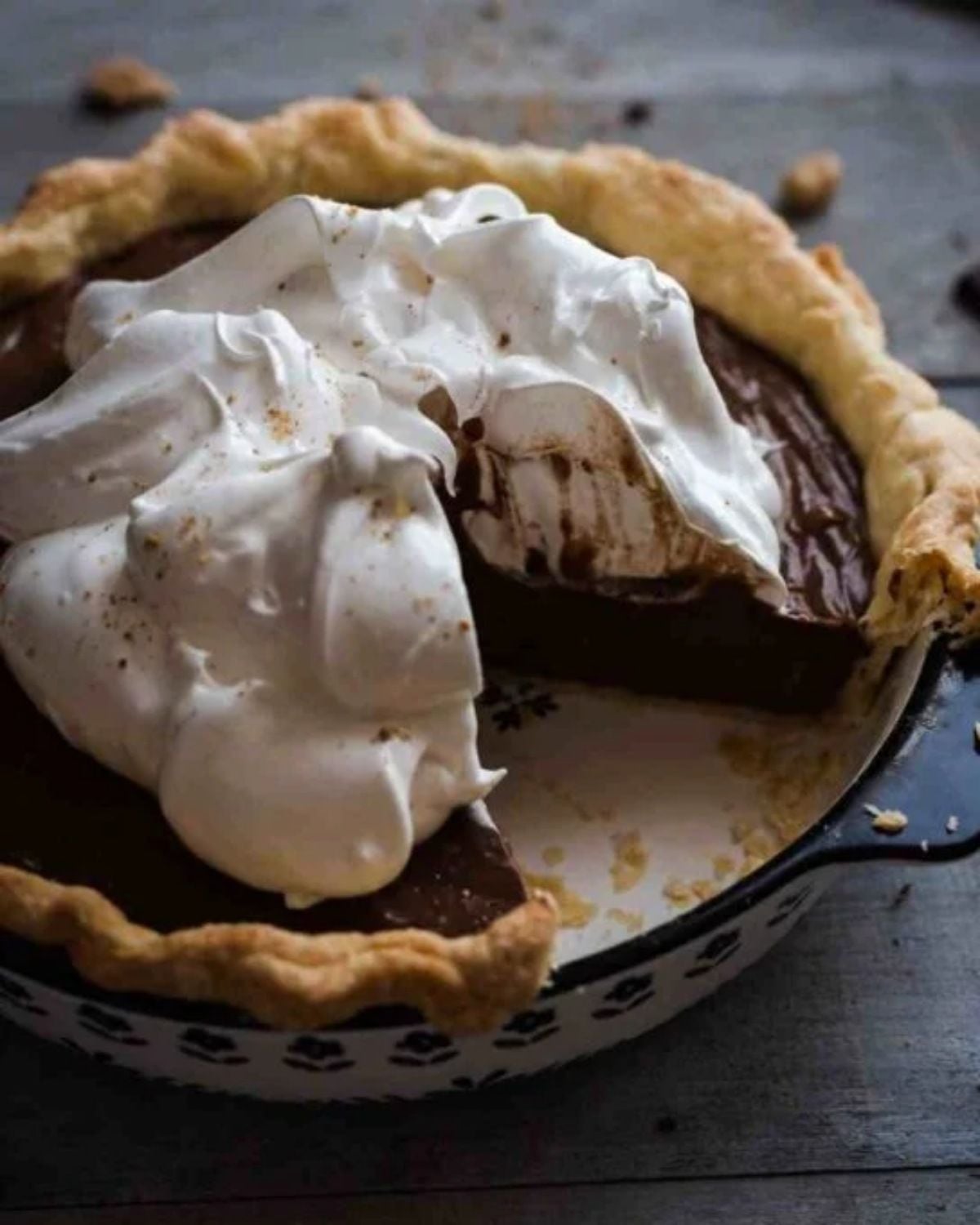 A rich chocolate cream pie topped with billowy whipped cream, with one slice removed to expose the dark pudding filling