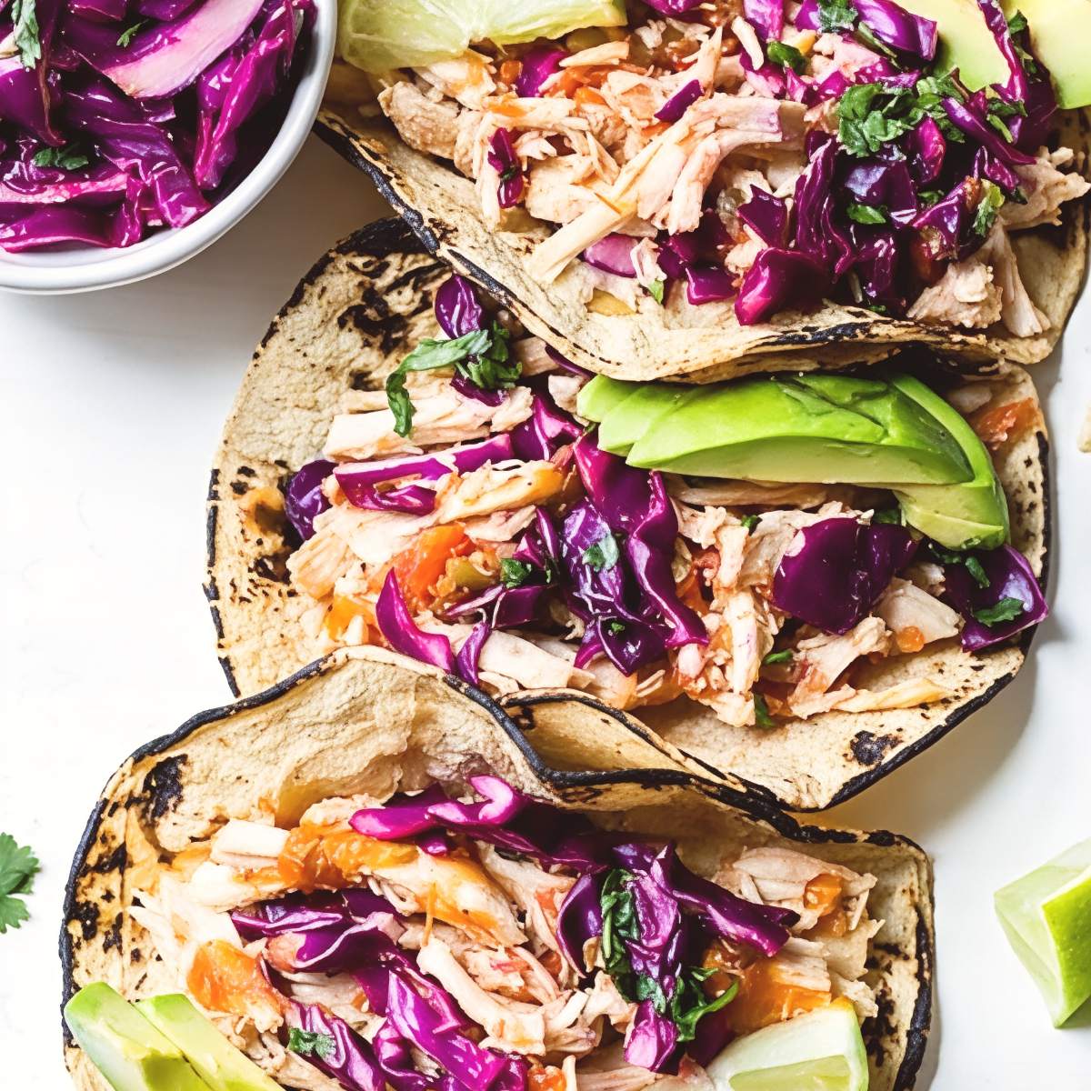 Soft corn tortillas filled with shredded slow-cooker chicken, fresh purple cabbage slaw, and avocado slices, making a quick and easy dump and go crockpot dinner (Lazy Dinner).