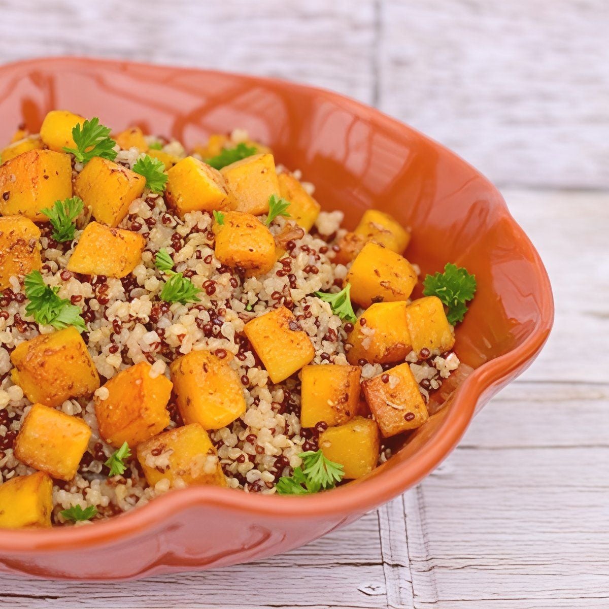 Healthy crockpot stuffing thanksgiving recipe made with quinoa, roasted butternut squash cubes, and fresh parsley served in an orange ceramic dish.