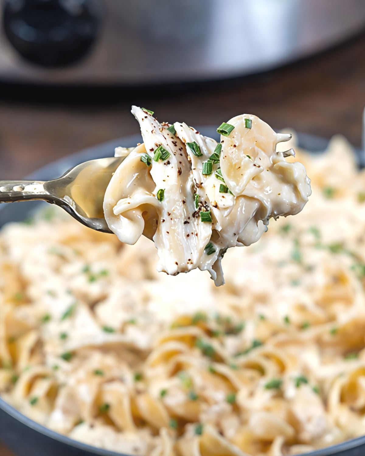 A fork lifts a creamy serving of ranch chicken and egg noodles topped with chives, showcasing an easy dump and go crockpot dinners chicken recipe.