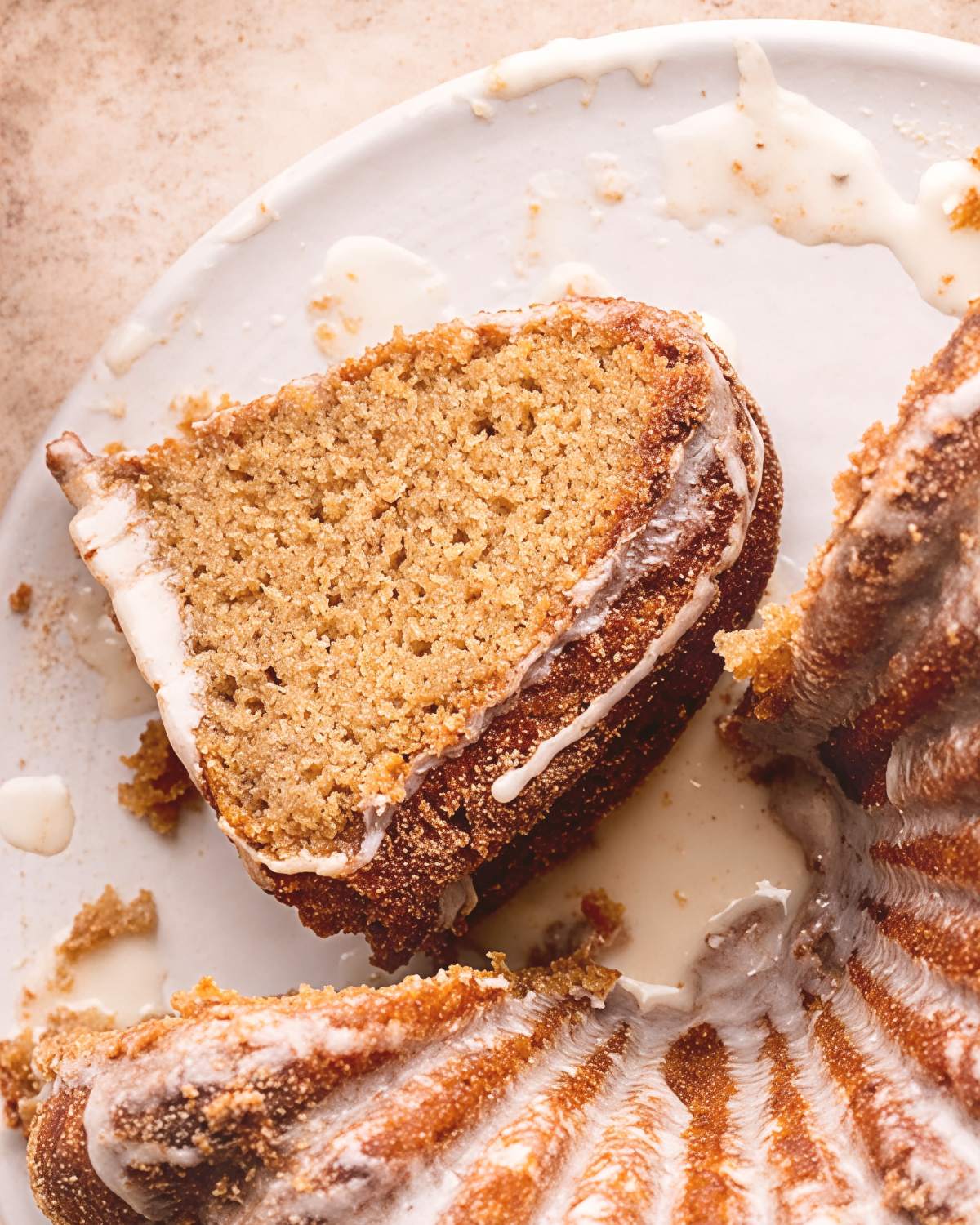 A slice of moist apple cider donut cake showing its soft crumb texture, coated in cinnamon sugar and drizzled with a sweet white glaze on a ceramic serving plate.