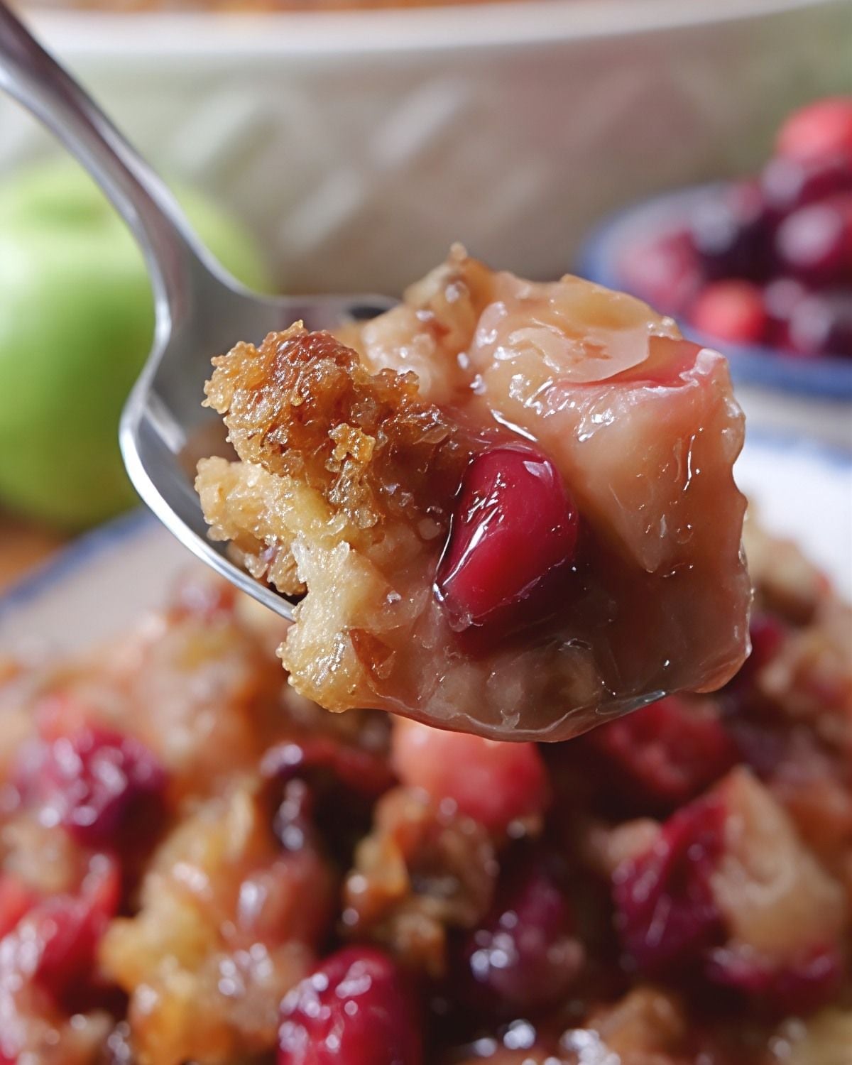 A close-up spoon scoop of warm apple cranberry cobbler showing tender spiced apples, tart whole cranberries, and a golden buttery brown sugar pecan topping