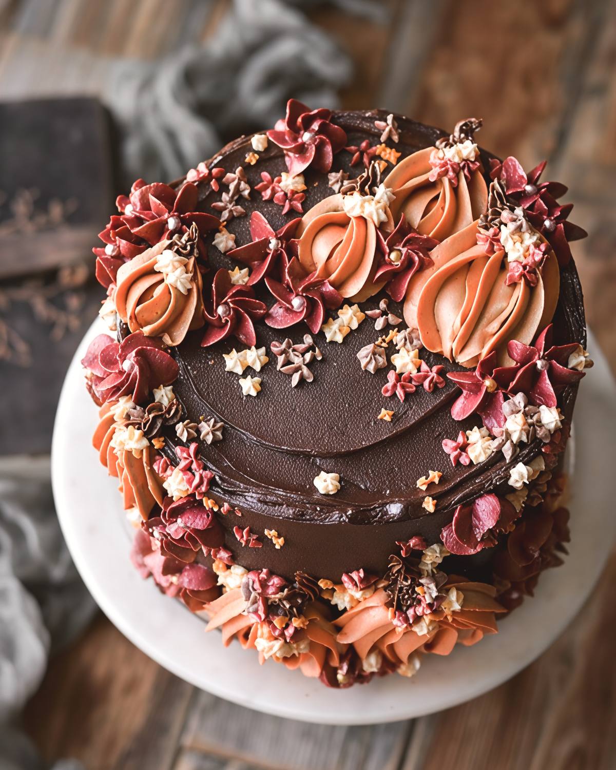 Rich chocolate Thanksgiving cake elegantly decorated with piped orange buttercream pumpkins and deep burgundy autumn flowers.