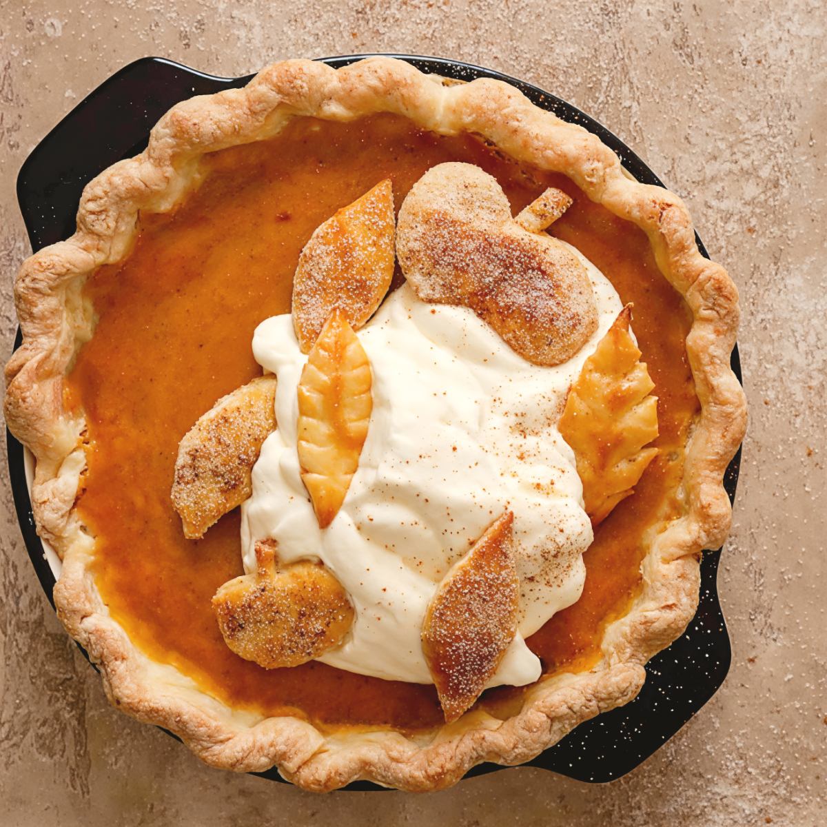 A freshly baked homemade pumpkin pie with a golden flaky crust, generously topped with fluffy whipped cream and decorative leaf-shaped pie crust cutouts.