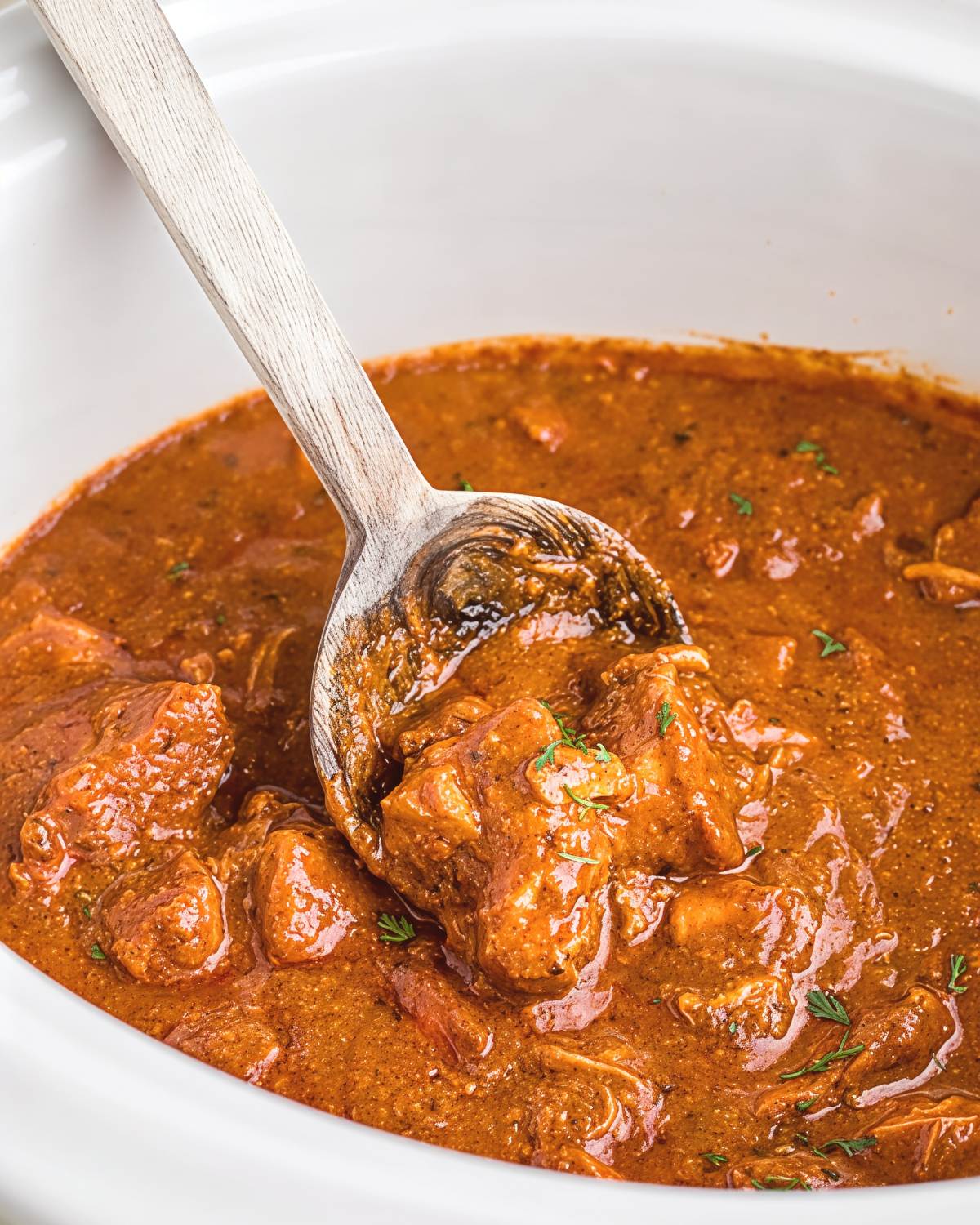 A wooden spoon scooping up rich, creamy chicken curry from a slow cooker, making an effortless dump and go crockpot dinner (Lazy Dinner).