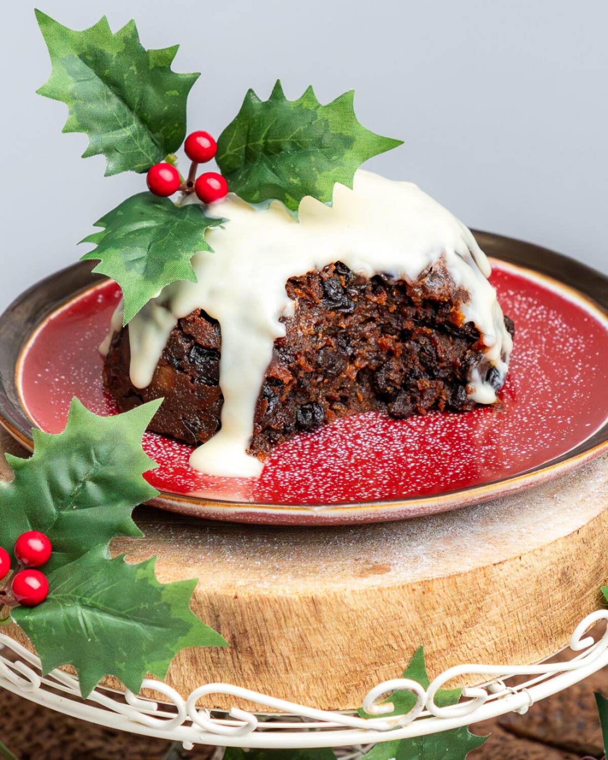 Traditional Irish Christmas pudding topped with creamy brandy sauce and a sprig of holly, served on a festive plate as a classic European Christmas dessert.