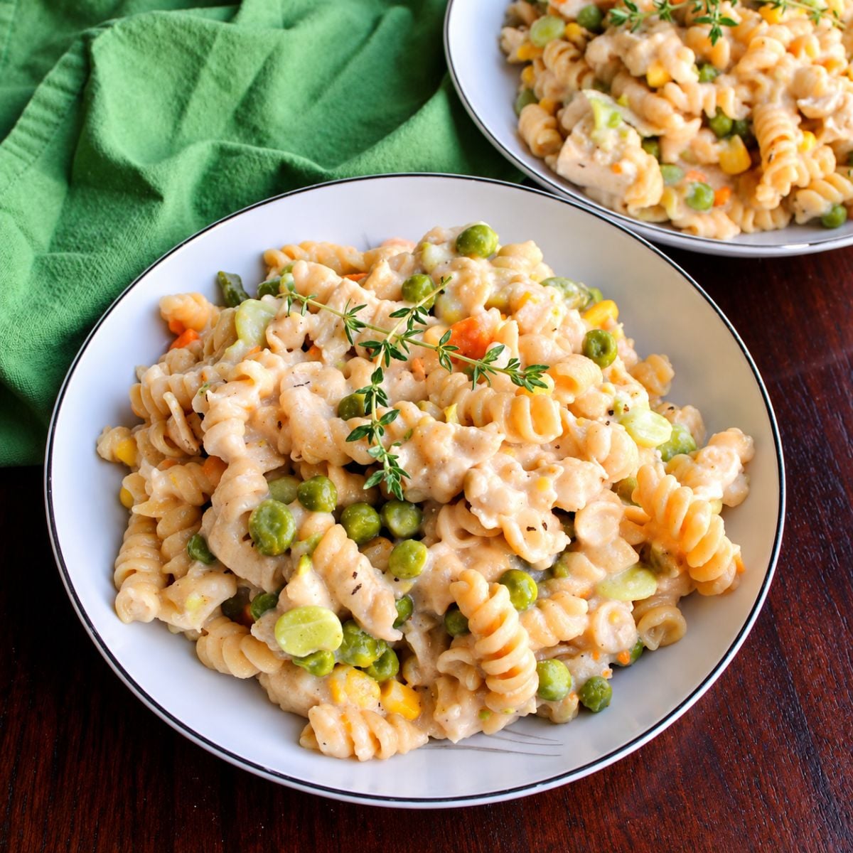 creamy chicken noodles in white serving dishes on a wooden table with a green towel alongside the dishes