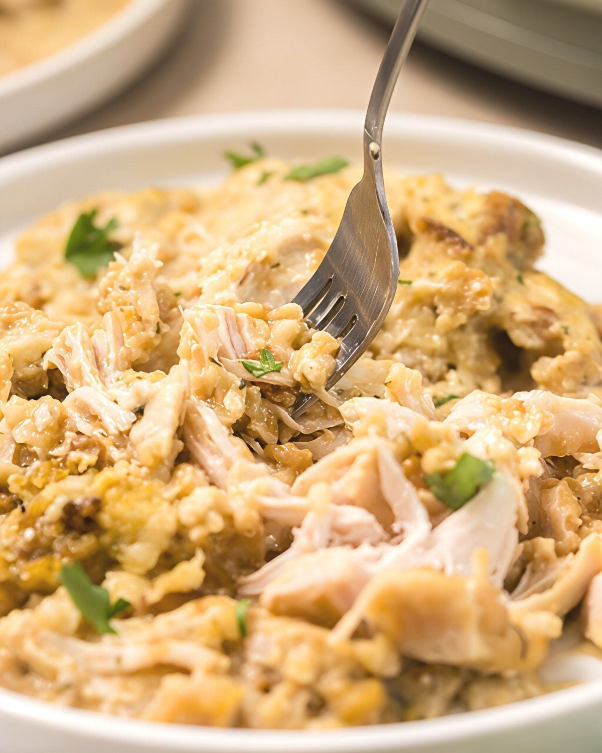 Comforting crockpot stuffing thanksgiving casserole made with shredded turkey, herbs, and gravy served in a white bowl with a fork.