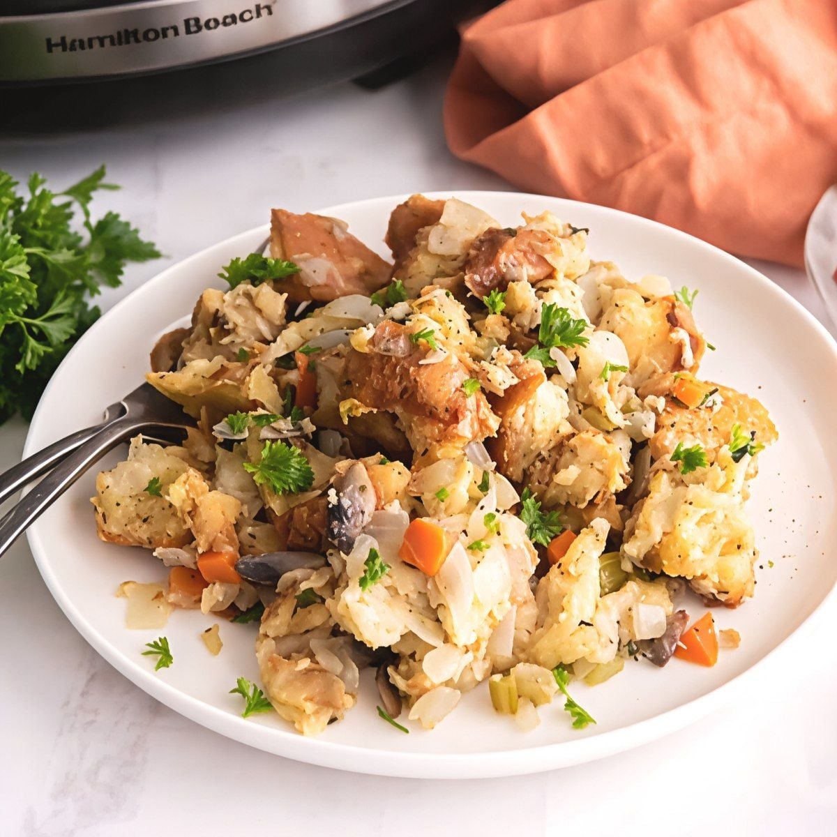 Flavorful crockpot stuffing thanksgiving recipe served on a white plate with fresh parsley next to a digital slow cooker.