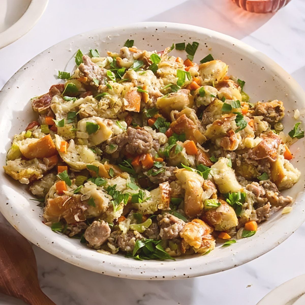 Savory crockpot stuffing thanksgiving recipe made with crumbled sausage, diced carrots, and chopped fresh parsley served in a large ceramic bowl.