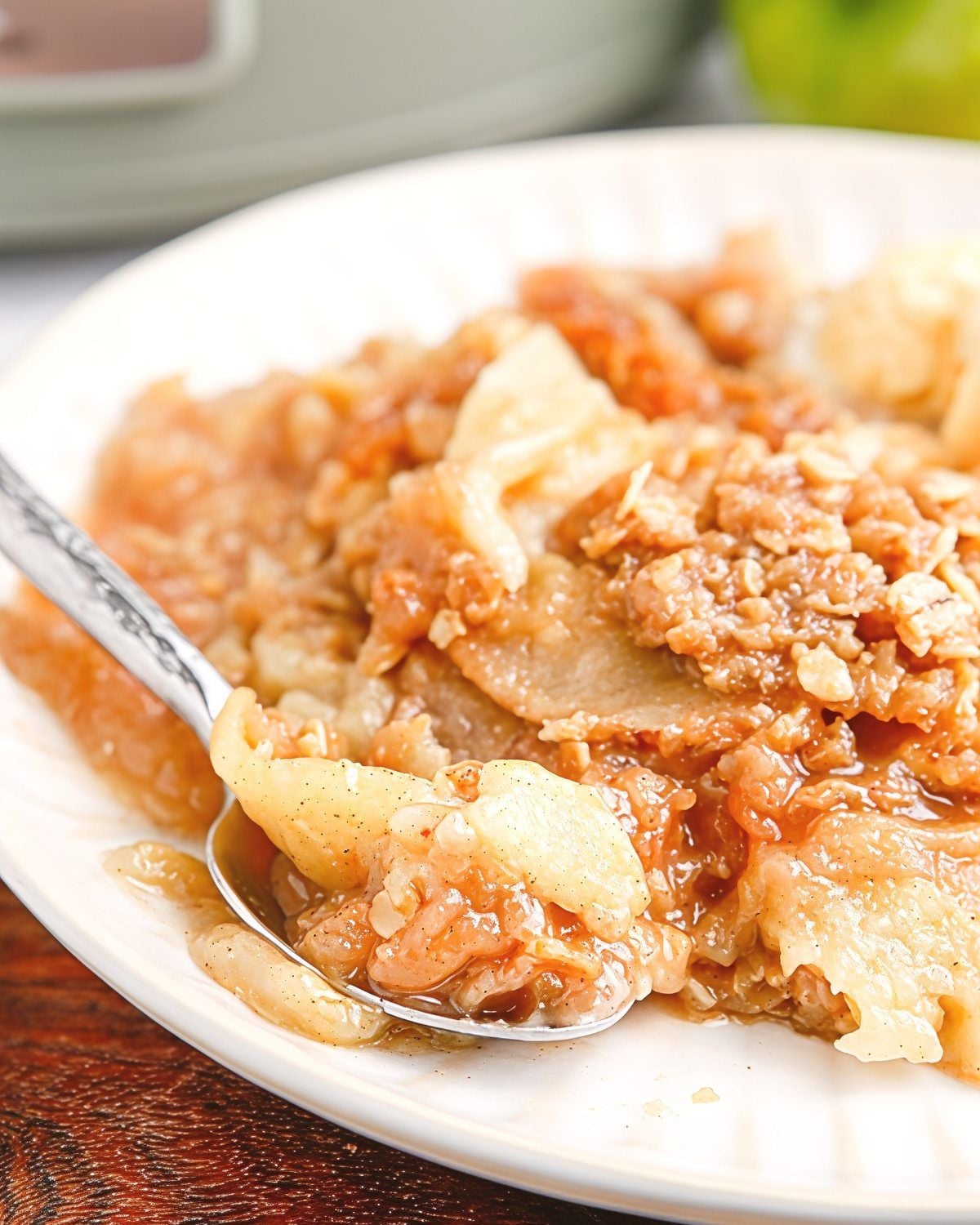 Warm crockpot apple crisp featuring tender sliced apples with an oat crumble topping served on a white plate, perfect for crockpot thanksgiving recipes.