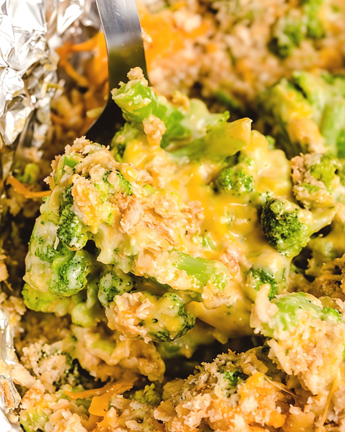 Spoon scooping cheesy broccoli crockpot casserole topped with melted cheddar and crushed Ritz crackers, perfect for crockpot thanksgiving recipes.