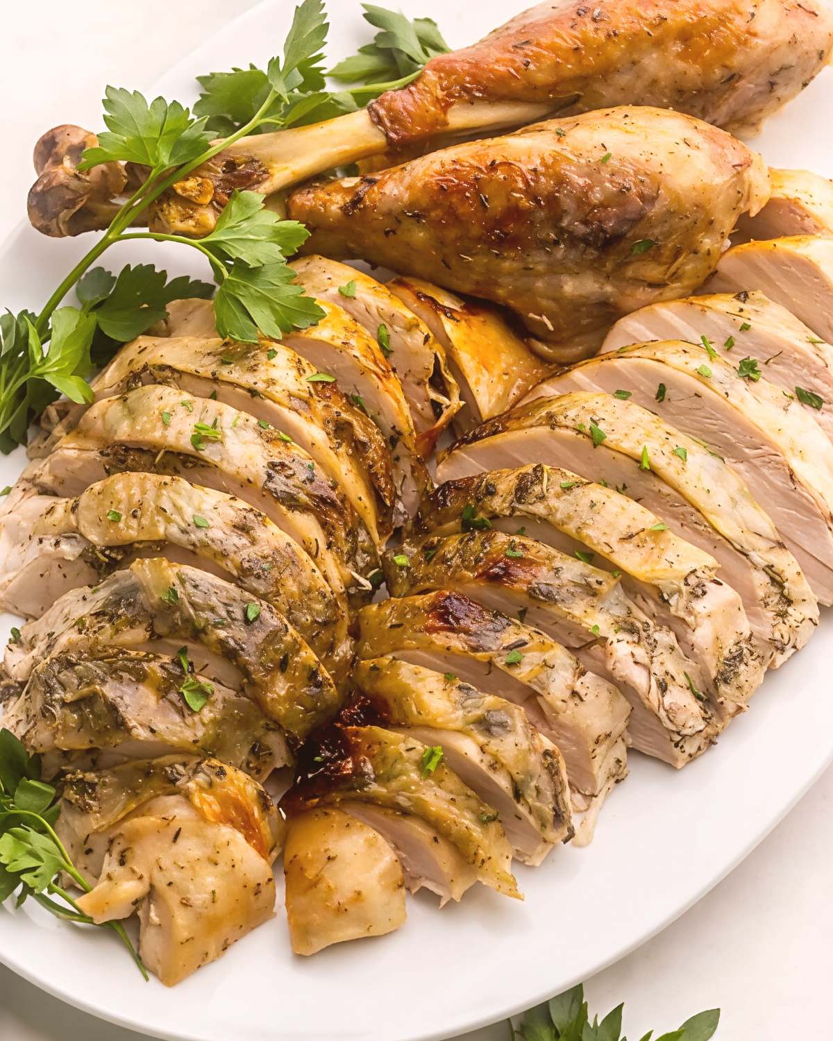Sliced crockpot turkey seasoned with garlic butter and fresh parsley served on a white platter, perfect for crockpot thanksgiving recipes.
