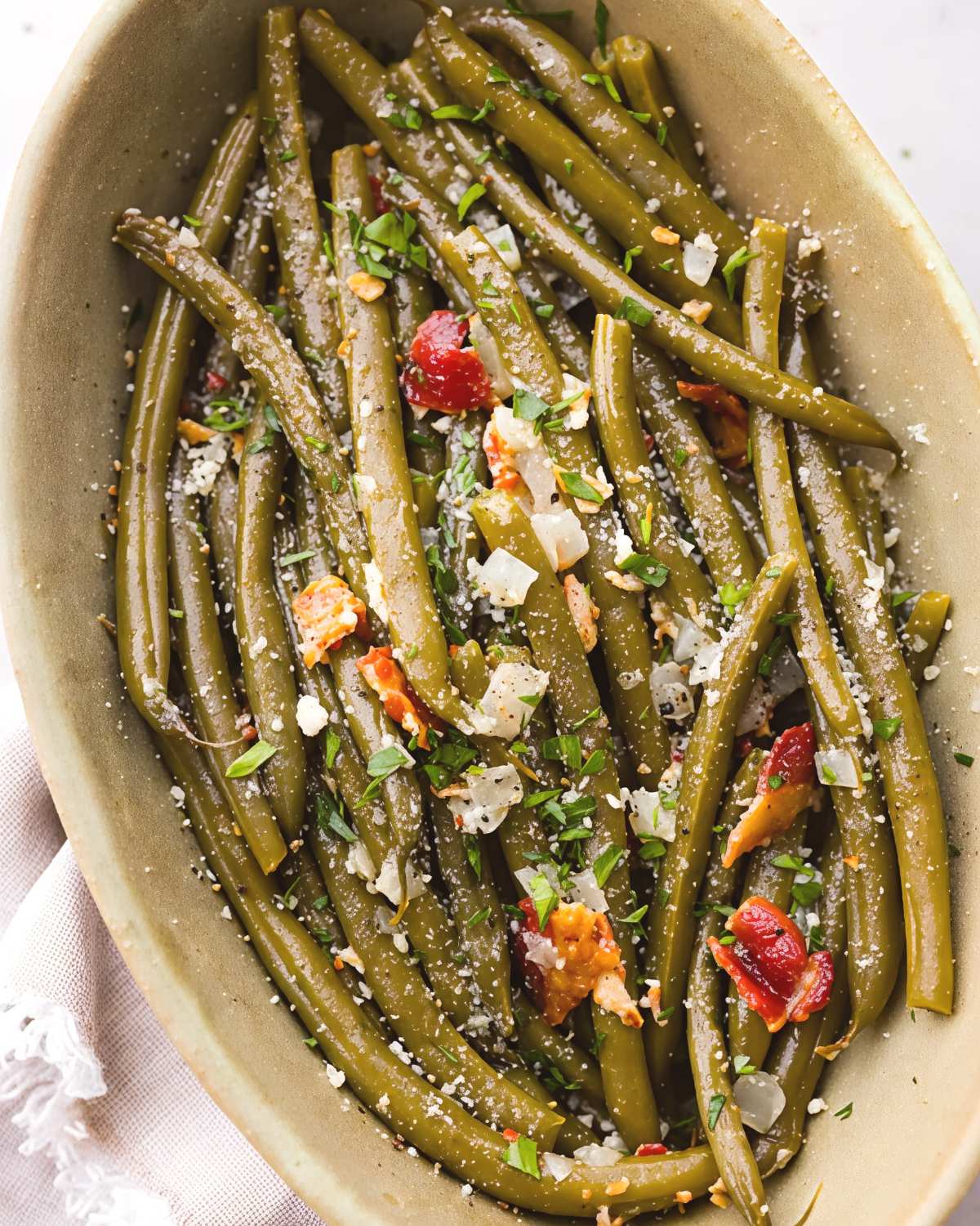 Tender crockpot green beans tossed with bacon, garlic, herbs, and parmesan cheese served in an oval bowl, perfect for crockpot thanksgiving recipes.