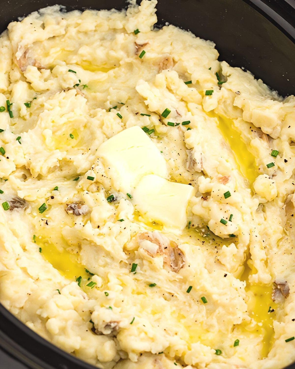 Creamy crockpot mashed potatoes topped with melting butter and fresh chives inside a slow cooker, perfect for crockpot thanksgiving recipes.