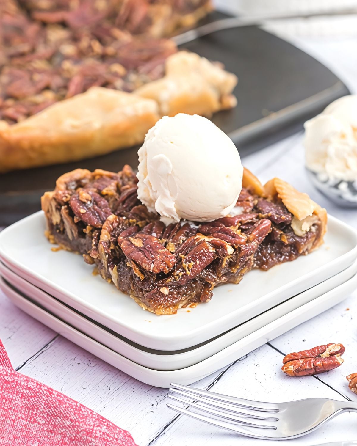 A square of Pecan Pie on a plate stacked on top of 2 additional plated